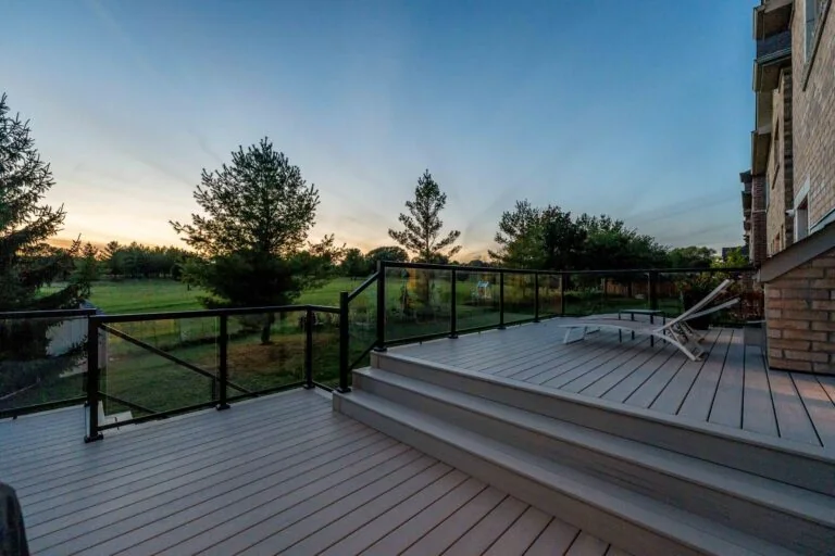Composite deck with glass railing overlooking a landscaped backyard at sunset
