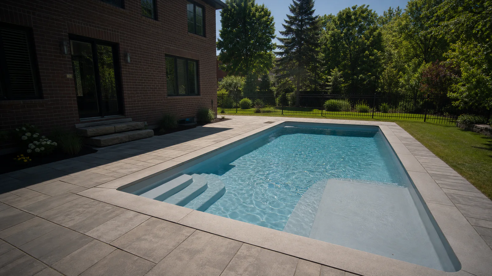 Rectangular fiberglass pool with integrated steps and lounging ledge beside a Greater Toronto Area brick home