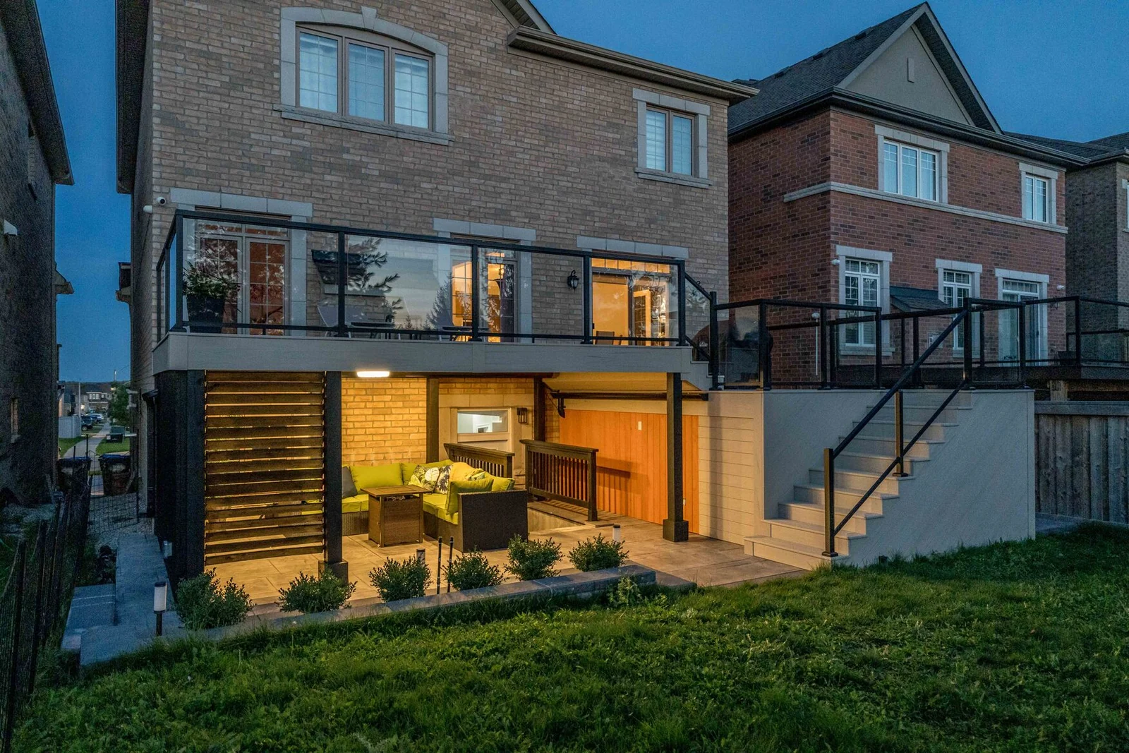 Two-tier composite deck and warmly lit covered lounge at a Bradford brick home at dusk