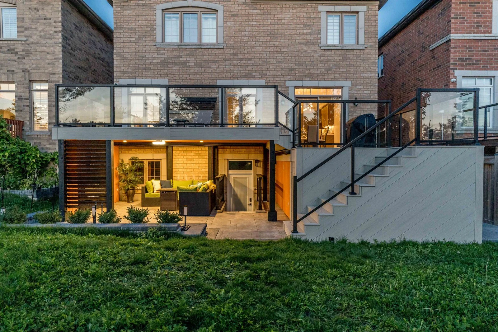 Two-tier composite deck with glass railings, wide stairs and an illuminated covered patio in Bradford