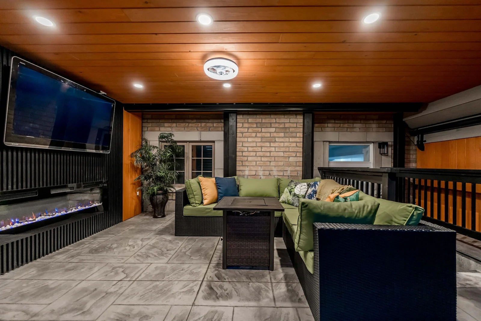 Covered outdoor entertainment area with hardscape floor, fireplace, television and sectional seating in Bradford
