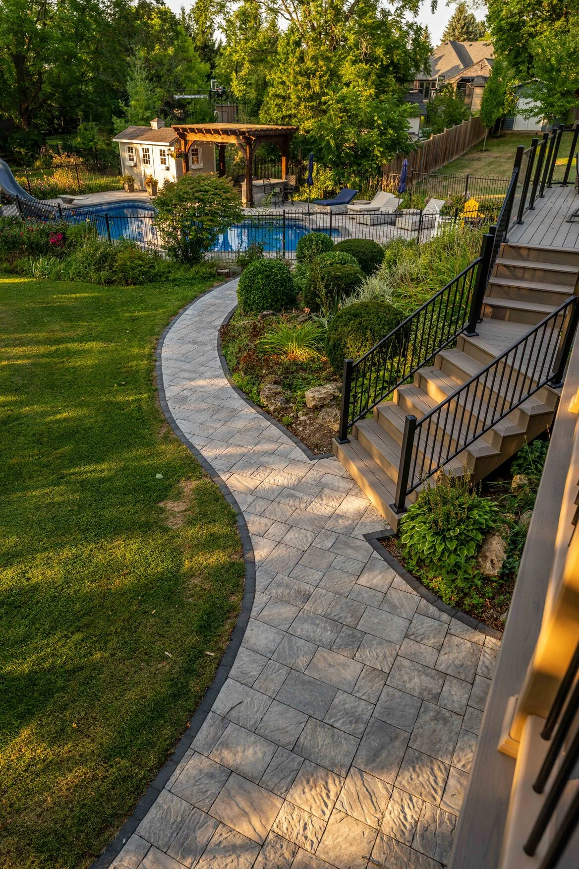 Curved stone path connecting a multi-level composite deck to the pool area in Schomberg