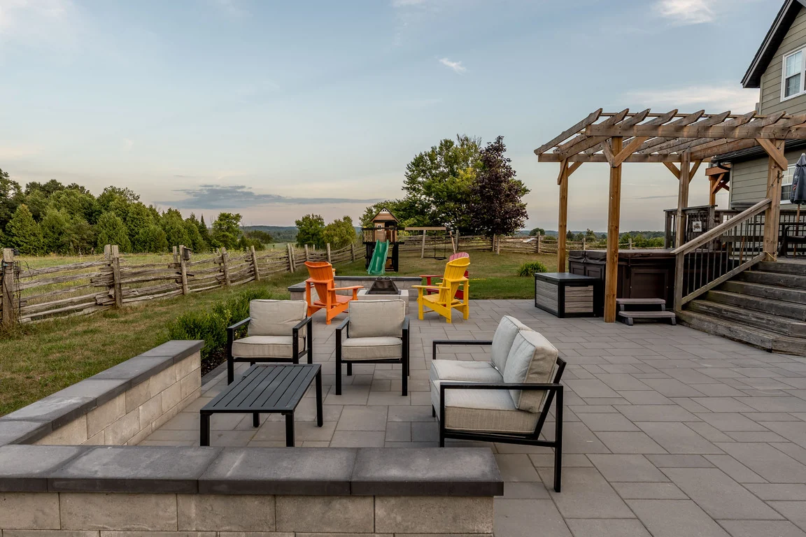 Hardscape patio lounge and fire-pit seating framed by low stone walls in an Innisfil backyard