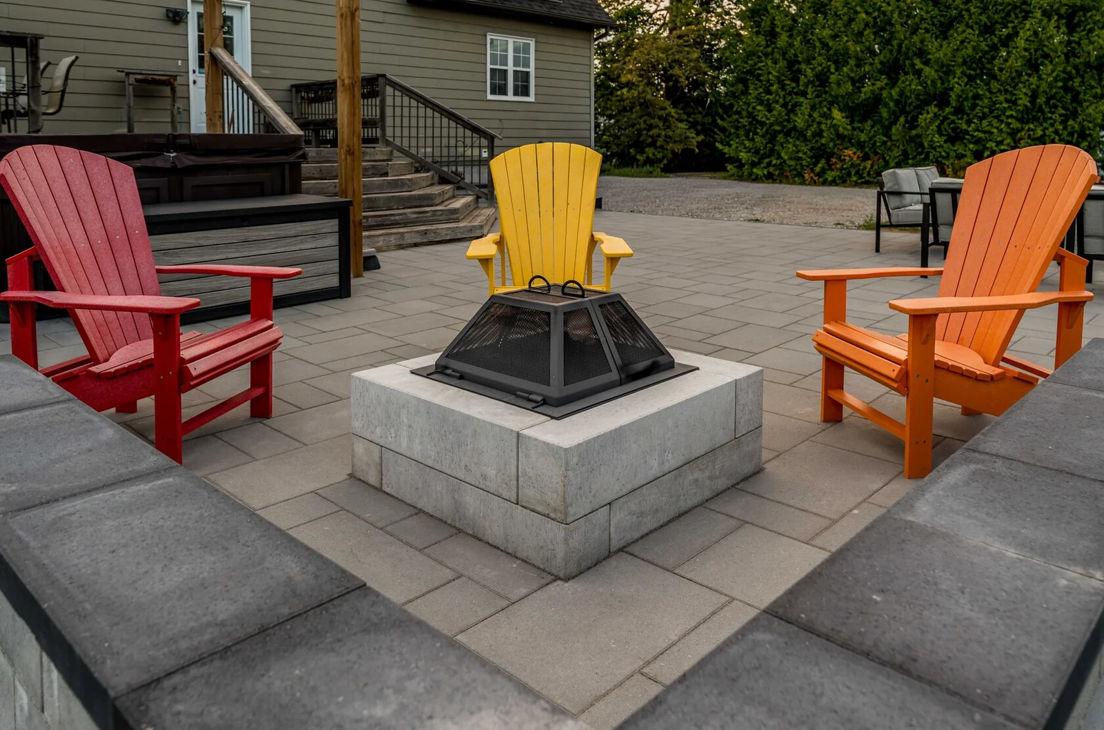 Square stone fire pit surrounded by colourful outdoor chairs on an Innisfil patio