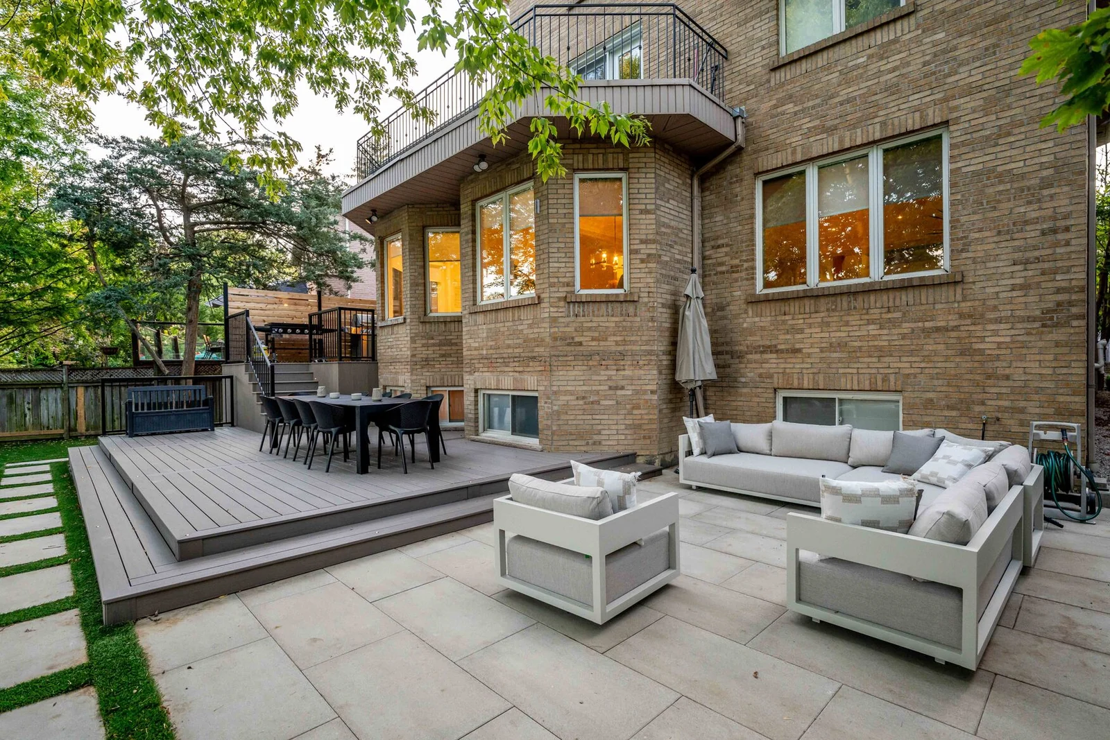 Multi-level grey composite deck beside a large-format stone lounge patio at a North York brick home