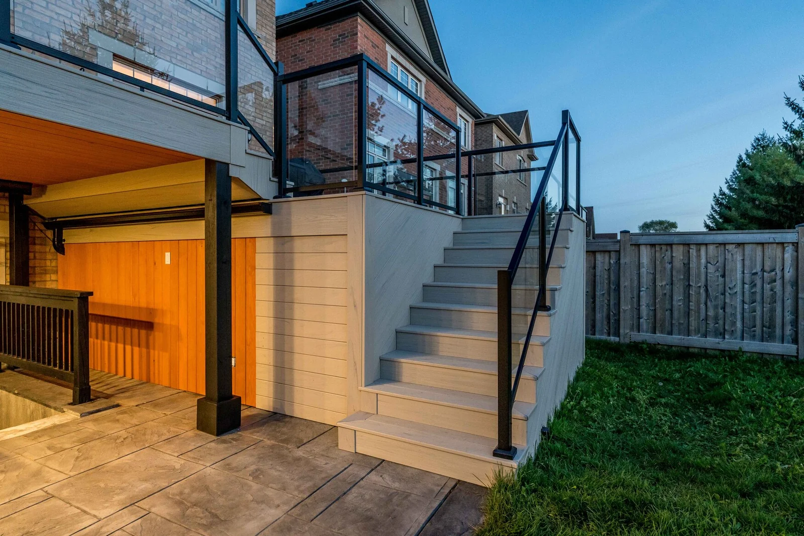Exterior composite staircase with glass guards connecting a two-tier Bradford deck to the hardscape patio